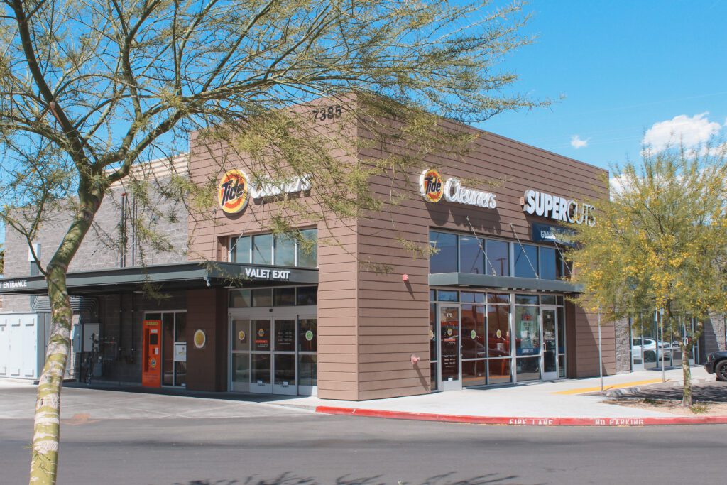 The exterior of a wood paneled and cinderblock Tide Cleaners and Supercuts store front.  